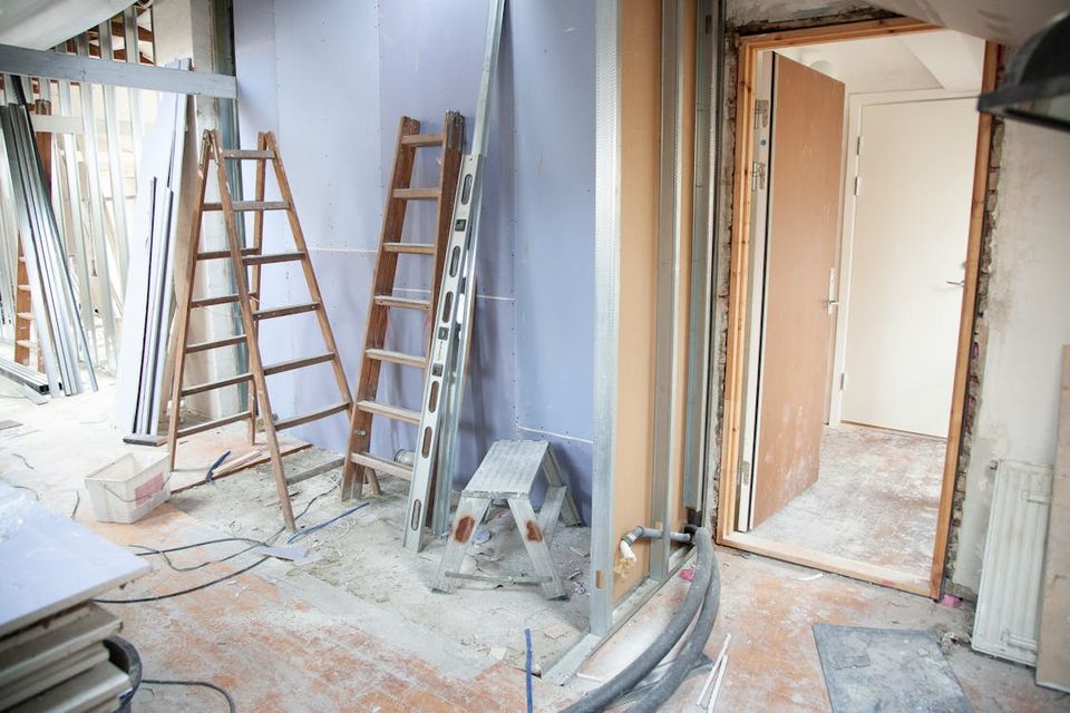 Homeowner photographing a mid-renovation kitchen with exposed framing and new electrical for documentation purposes