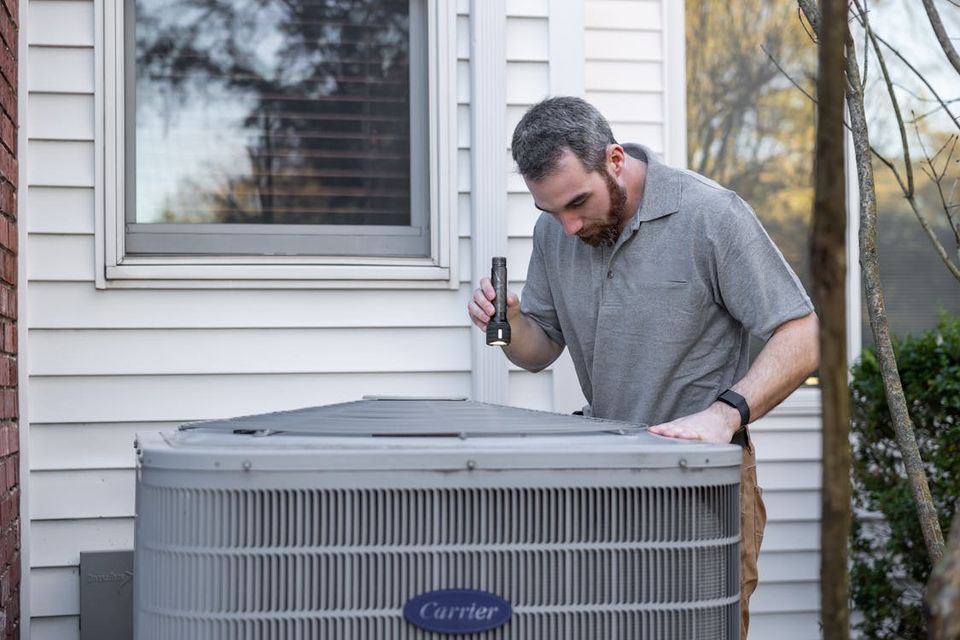 Homeowner logging a repair entry on a tablet while a technician works on an HVAC unit in the background