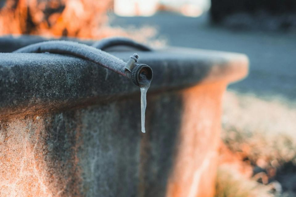 Frozen outdoor faucet with icicle and foam-insulated hose showing winter pipe protection