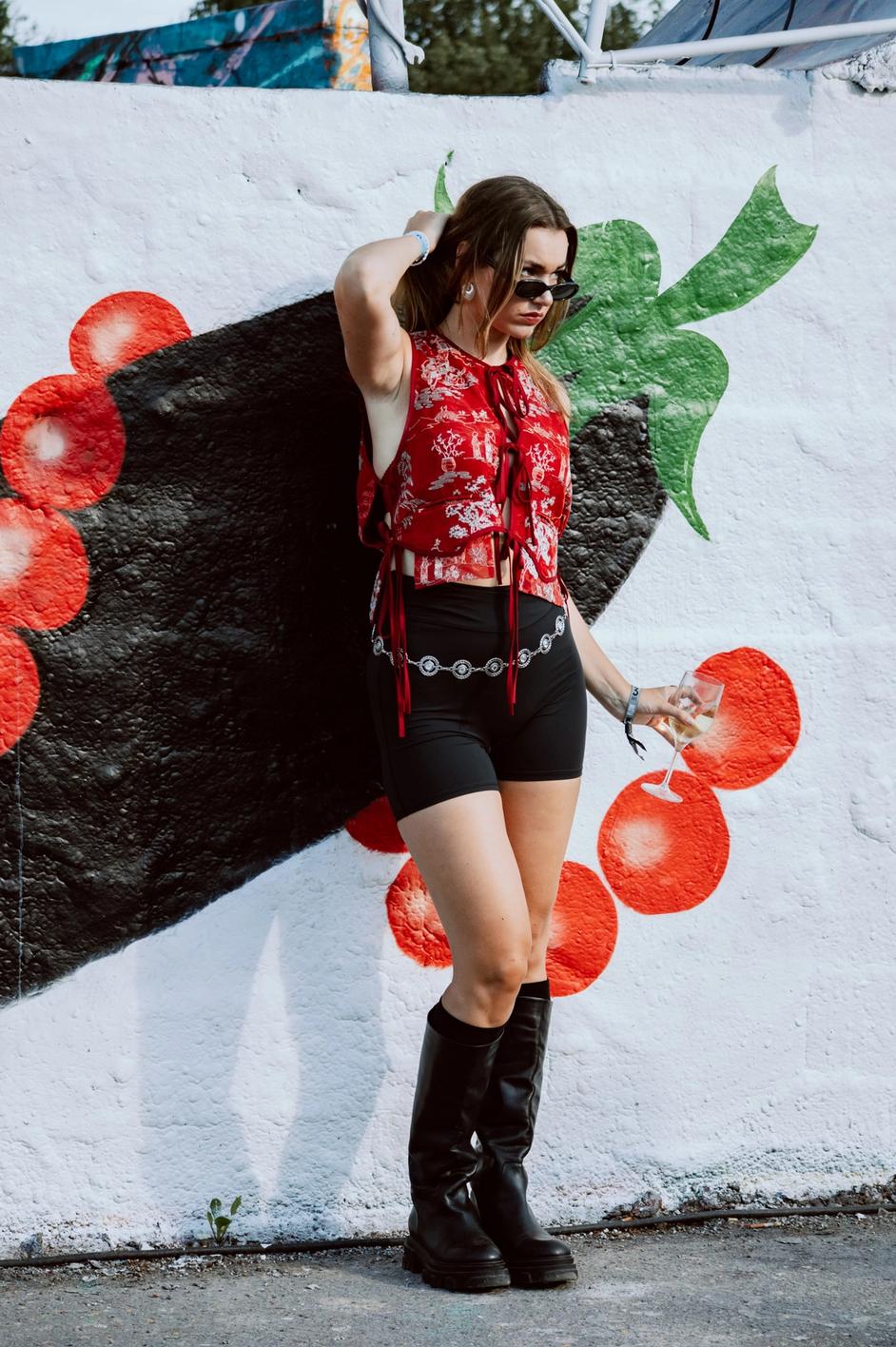 Девушка у стены с ярким граффити, в красном топе и чёрных шортах (Nainen graffitiseinän edessä punaisessa topissa ja mustissa shortseissa).