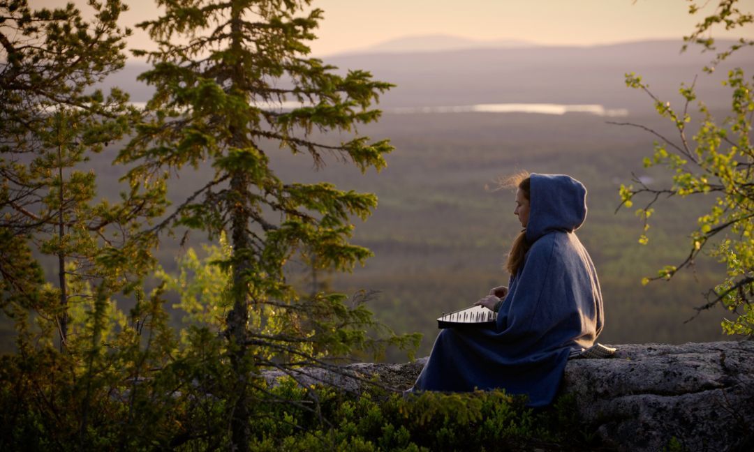 Henkilö istuu kallion päällä metsämaisemassa ja katselee kaukaista maisemaa.