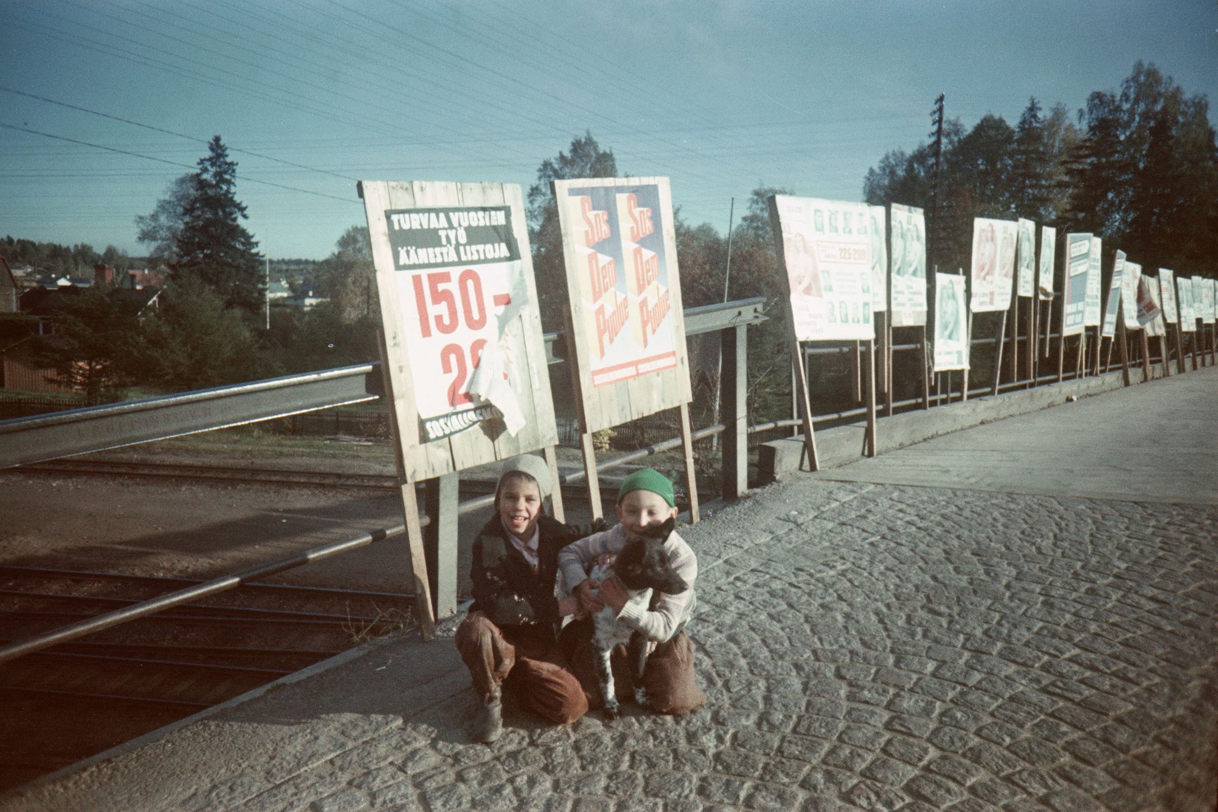 Kuva: Tuhka, A. Lapsia ja koira vaalimainosten edessä Helsingissä. Museovirasto.