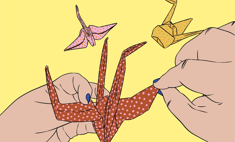Two hands folding a red polka-dotted origami crane, with two other completed cranes—one pink and one yellow—floating above, set against a yellow background