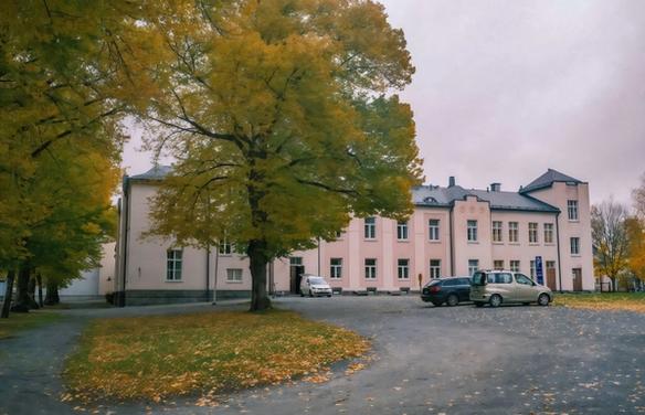 Здание с парковкой в окружении осенних деревьев (Rakennus ja pysäköintialue syksyisten puiden ympäröimänä)