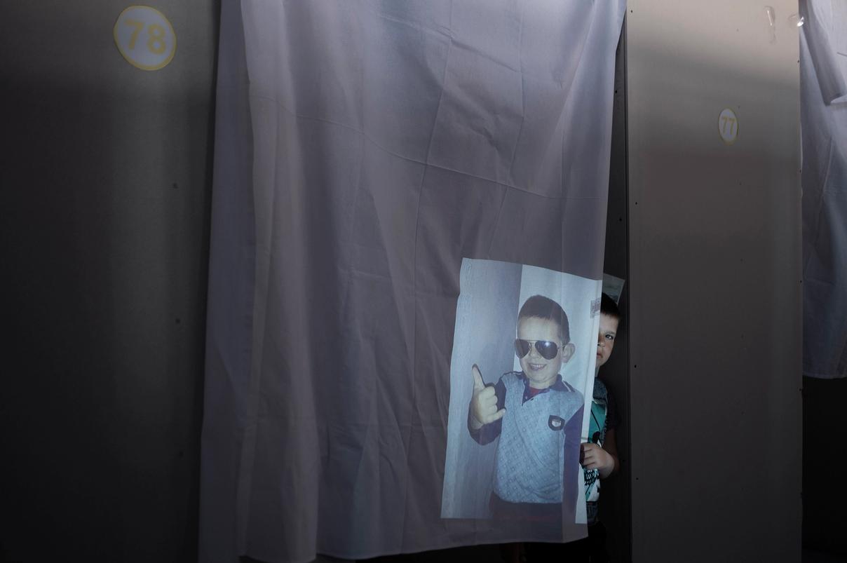 Мальчик выглядывает из-за занавески, на ткань проецируется его фото в солнечных очках (Poika kurkistaa verhon takaa, kankaalle heijastuu hänen kuvansa aurinkolaseissa)