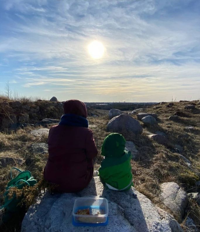 Иллюстрация: женщина и ребёнок сидят на камне (Kuvitus: nainen ja lapsi istuvat kivellä).