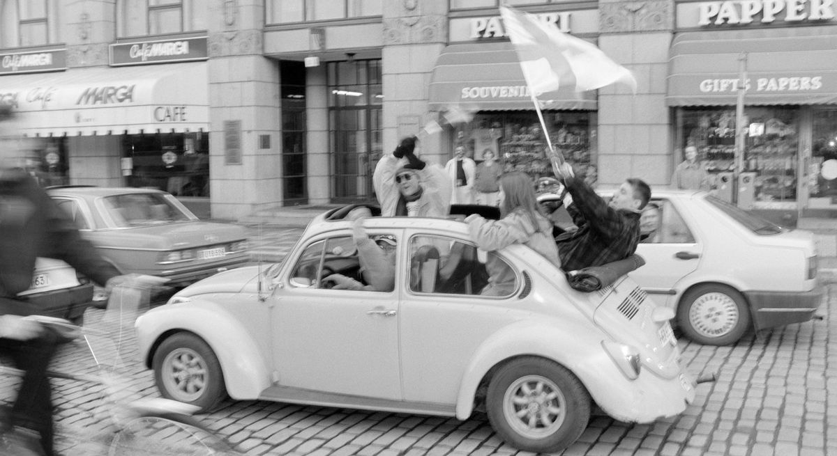 Люди празднуют и размахивают финским флагом в машине (Ihmiset juhlivat autossa heiluttaen Suomen lippua)