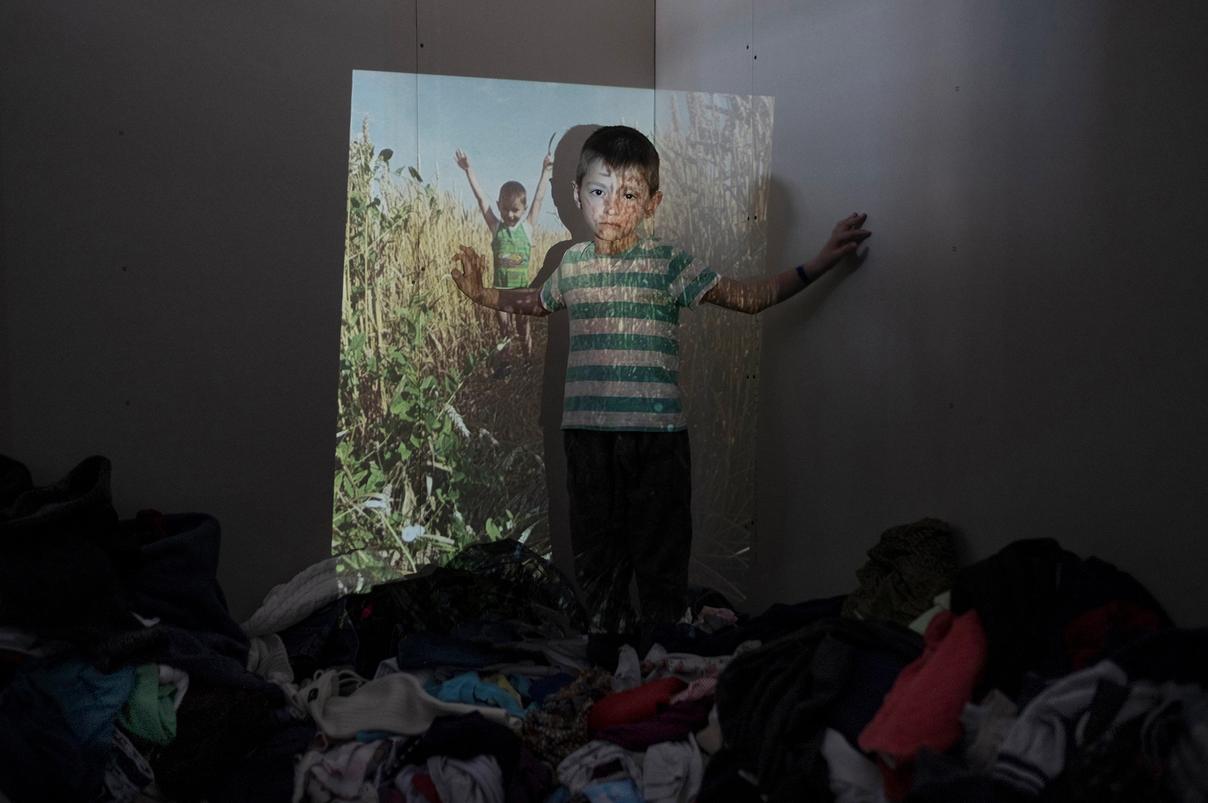 Мальчик стоит у стены с проекцией поля и детей / Poika seisoo seinää vasten, johon heijastetaan kuva pellosta ja lapsista
