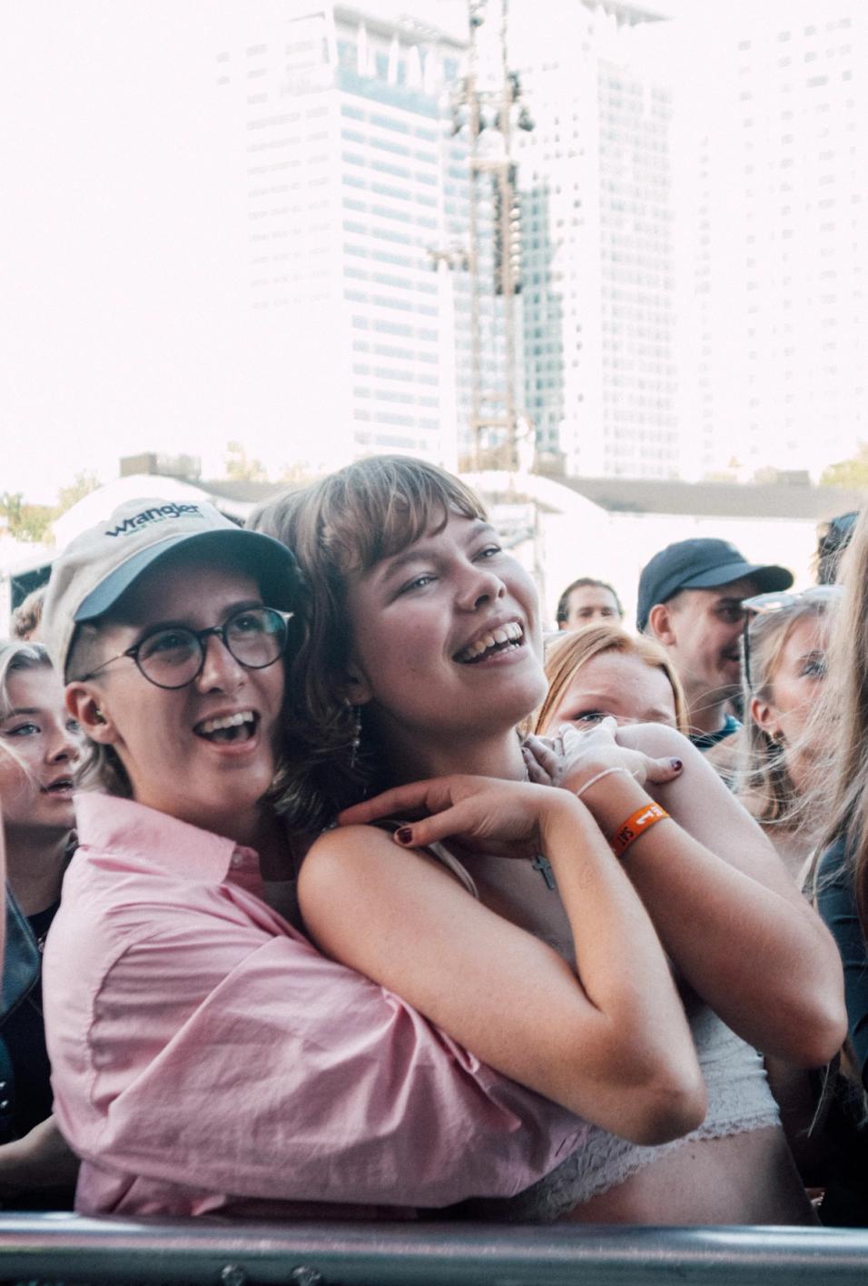 Две молодые женщины у сцены, улыбаются и обнимаются в толпе (Kaksi nuorta naista lavan edessä, hymyilevät ja halaavat).