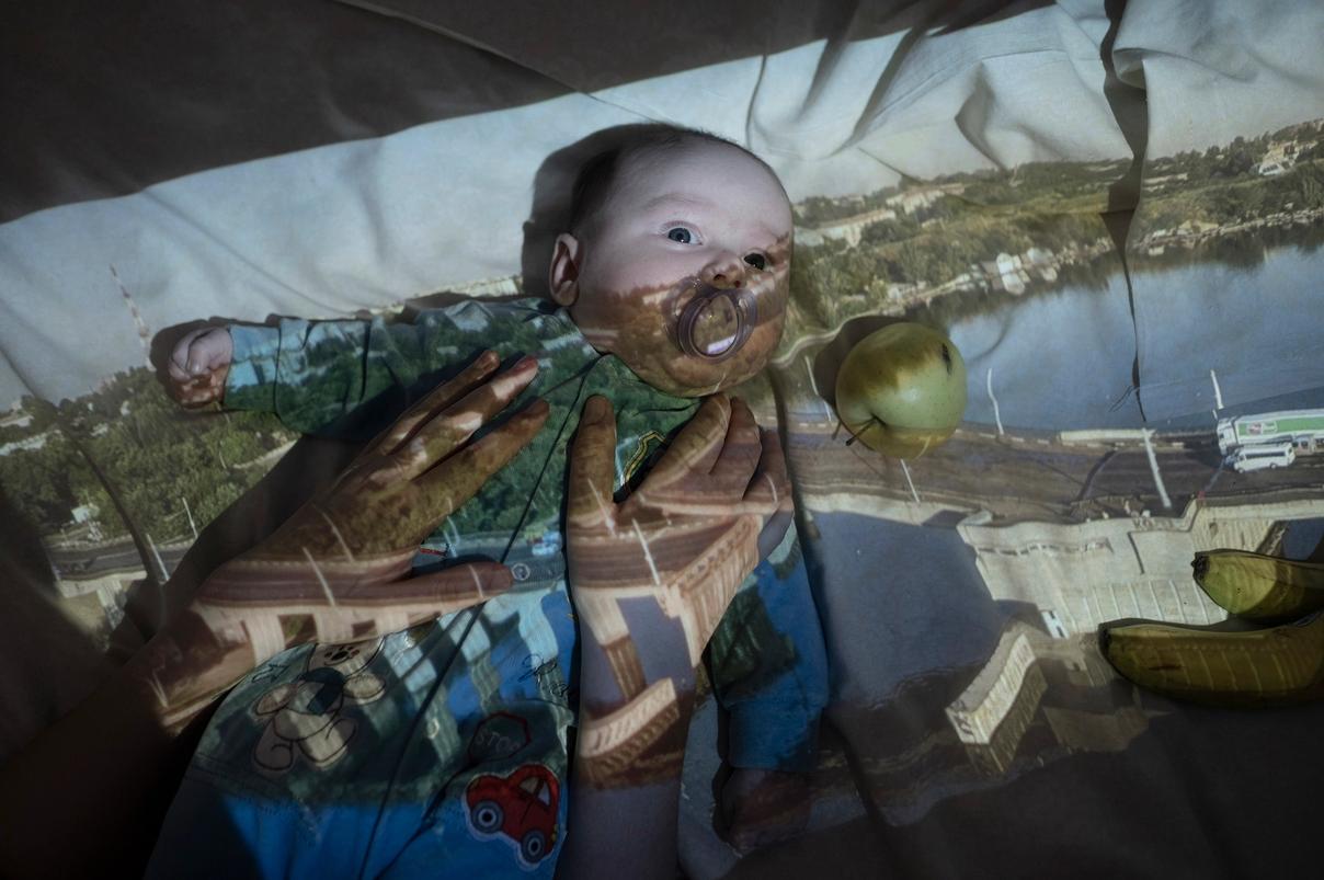 Младенец с пустышкой лежит с проекцией города на лице и теле (Vauva tutin kanssa makaa, kaupungin kuva heijastuu kasvoille ja vartalolle)