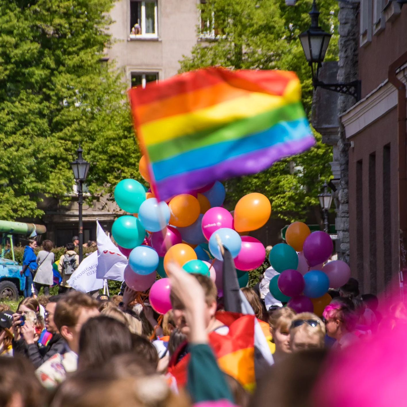 Участники Прайда с радужным флагом и яркими воздушными шарами. (Pride-osallistujia sateenkaarilipulla ja kirkkailla ilmapalloilla.)