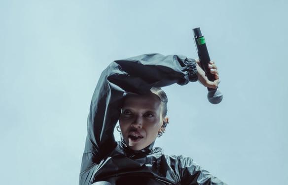 Певица на сцене в тёмном костюме с микрофоном в руке (Laulaja lavalla tummassa asussa mikrofonin kanssa).