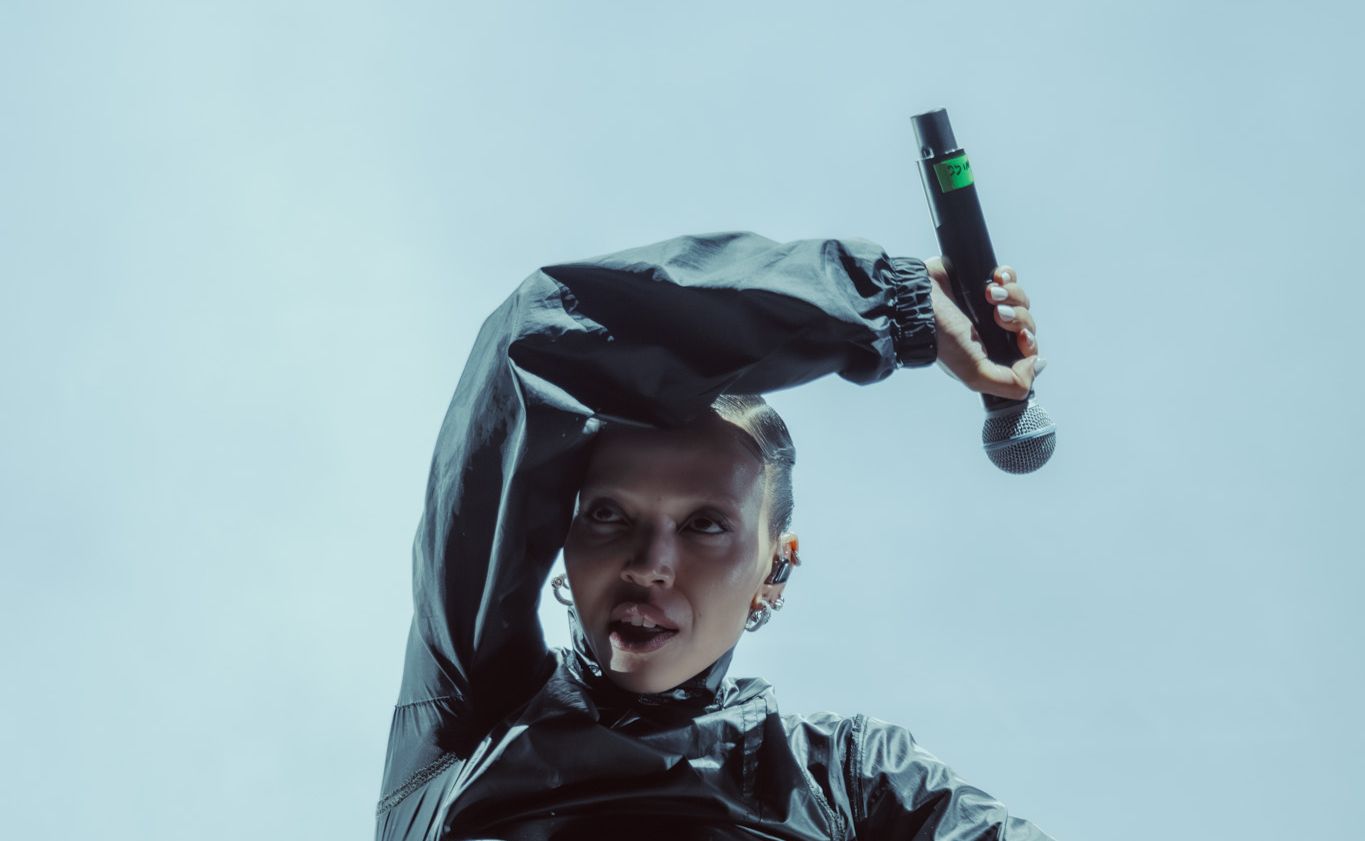 Певица на сцене в тёмном костюме с микрофоном в руке (Laulaja lavalla tummassa asussa mikrofonin kanssa).