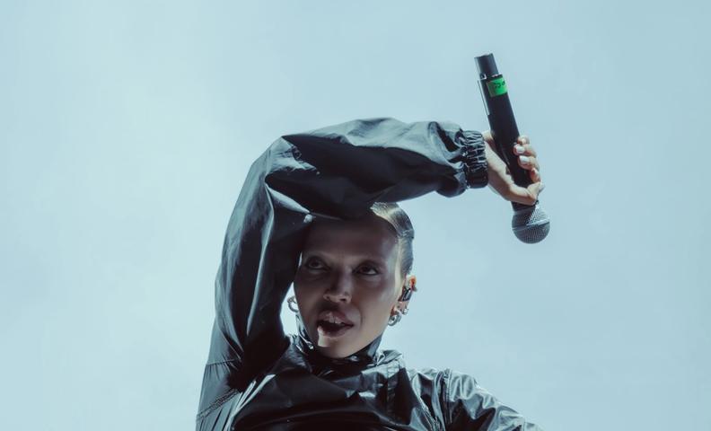 Певица на сцене в тёмном костюме с микрофоном в руке (Laulaja lavalla tummassa asussa mikrofonin kanssa).