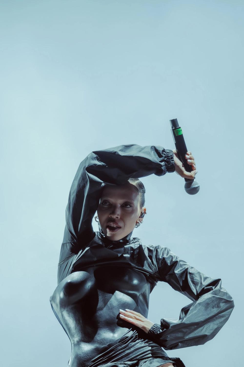 Певица на сцене в тёмном костюме с микрофоном в руке (Laulaja lavalla tummassa asussa mikrofonin kanssa).