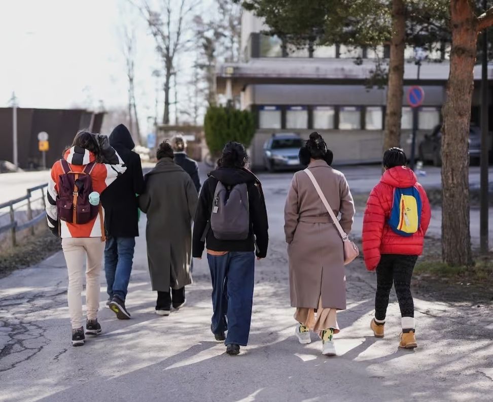 Группа людей идет по улице с рюкзаками, вид со спины (Ryhmä ihmisiä kävelee kadulla reput selässä, kuvattu takaa)