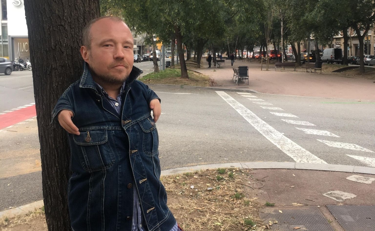 Мужчина стоит на улице, оперевшись на дерево (Mies seisoo kadulla puun runkoon nojaten)