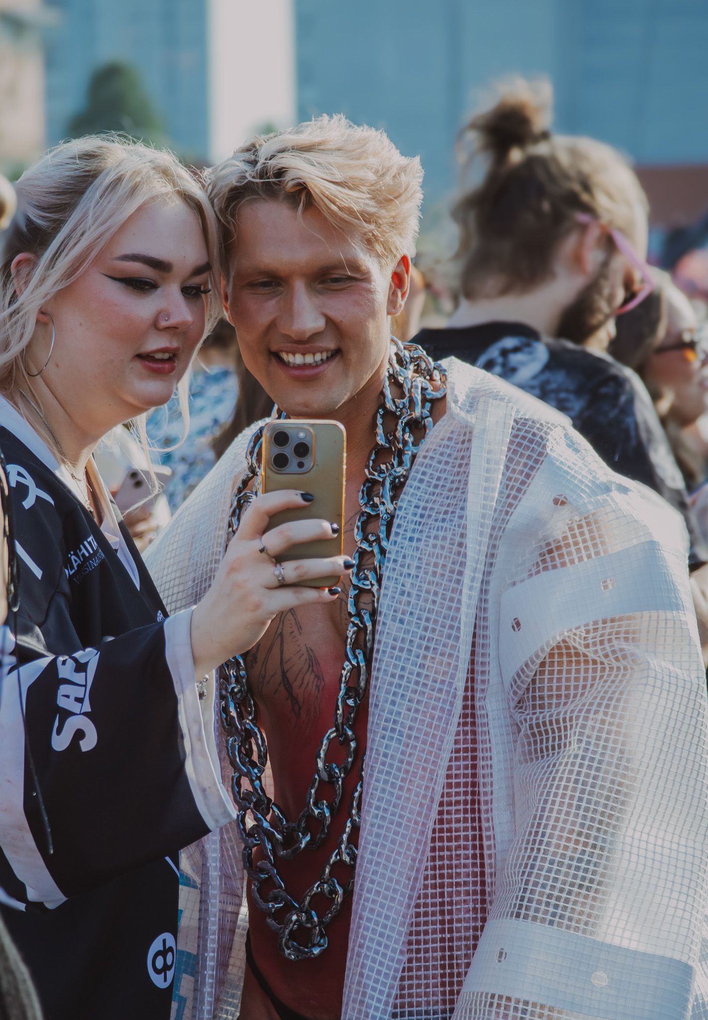 Двое молодых людей смотрят в телефон на фестивале (Kaksi nuorta katsoo puhelinta festivaalilla).