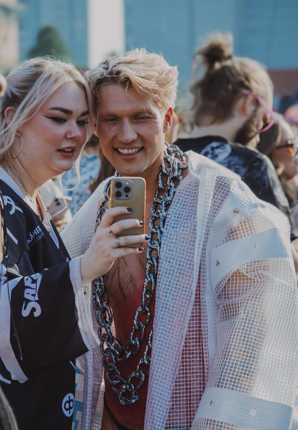 Двое молодых людей смотрят в телефон на фестивале (Kaksi nuorta katsoo puhelinta festivaalilla).