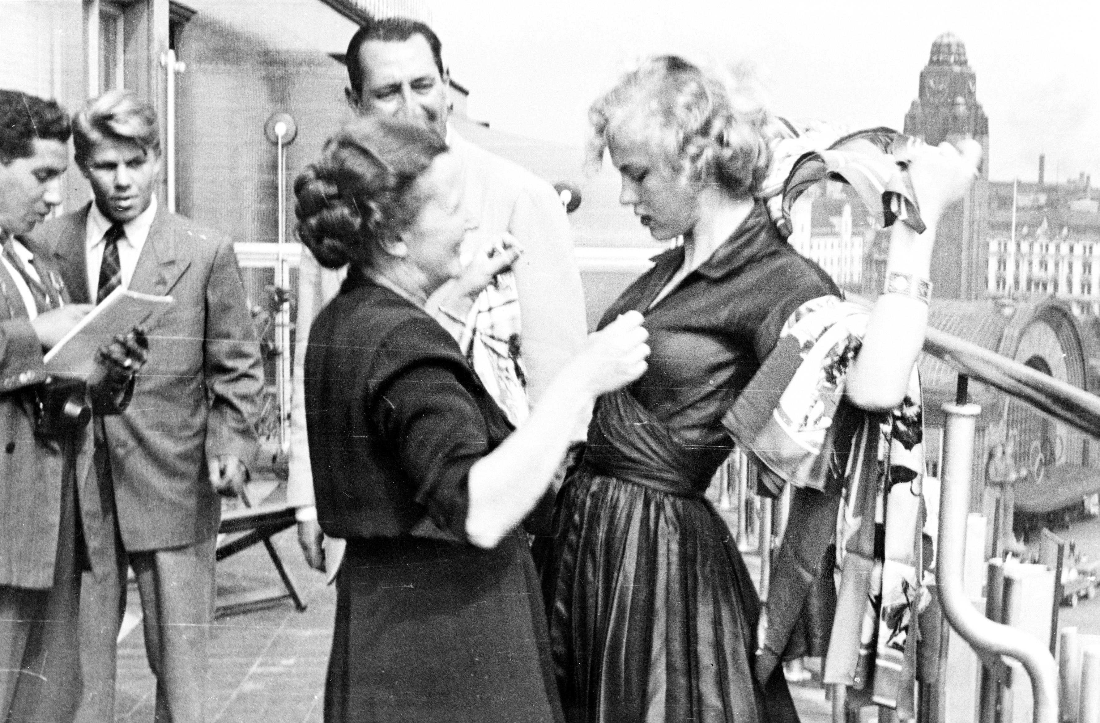 Женщина поправляет платье Арми Куусела на террасе ресторана (Nainen parantaa Armi Kuuselan asua ravintolan terassilla)