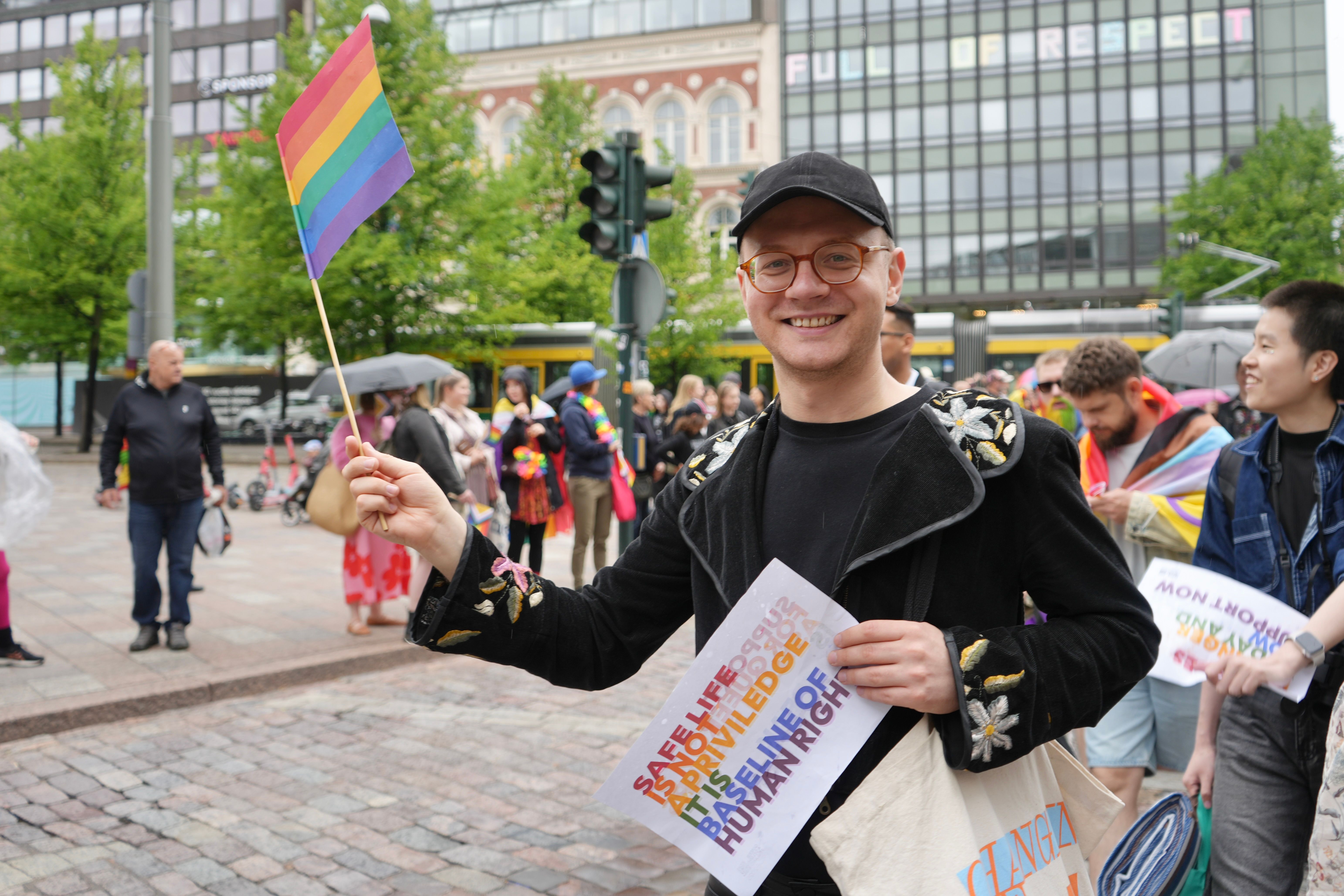 Участник Прайда в Хельсинки с радужным флагом и плакатом (Helsinki Pride -osallistuja sateenkaarilipulla ja kyltillä)