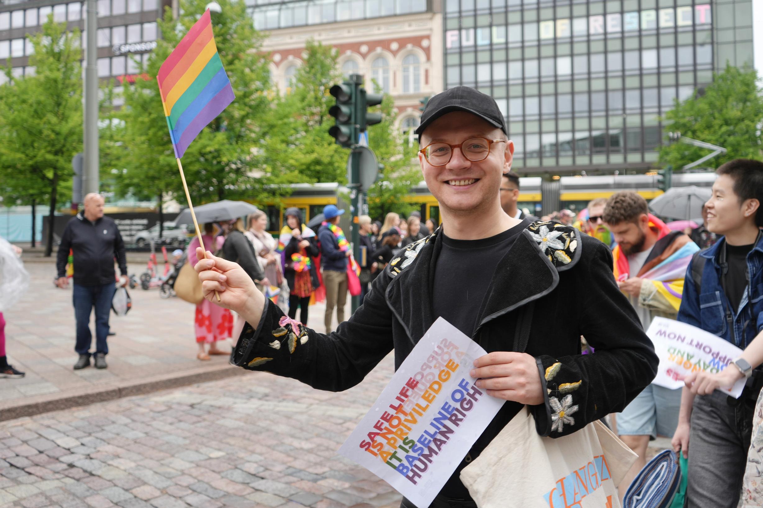 Участник Прайда в Хельсинки с радужным флагом и плакатом (Helsinki Pride -osallistuja sateenkaarilipulla ja kyltillä)