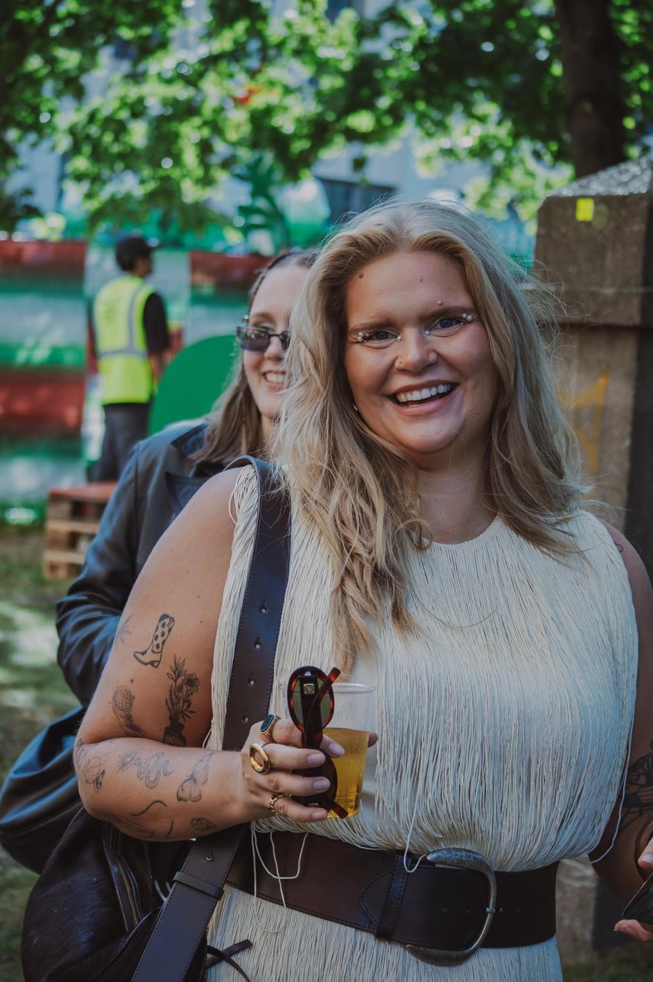 Женщина на фестивале улыбается, держит напиток в руке (Nainen festivaalilla hymyilee ja pitää juomaa kädessä).