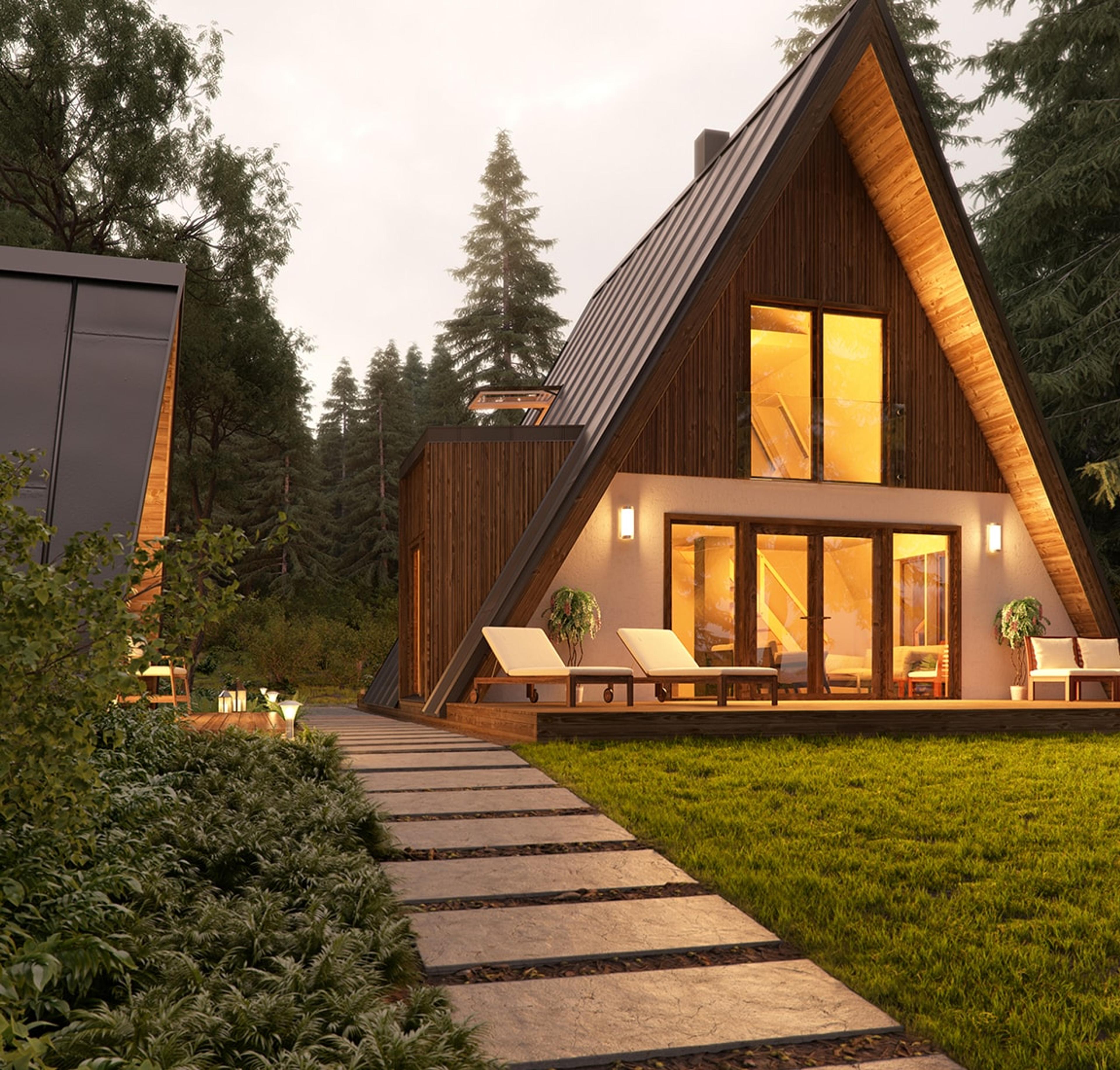 An architectural render shows a cozy Solo series A-frame house at dusk, featuring glowing interior lights, dark wood siding, a small side dormer, and an inviting deck with lounge chairs.