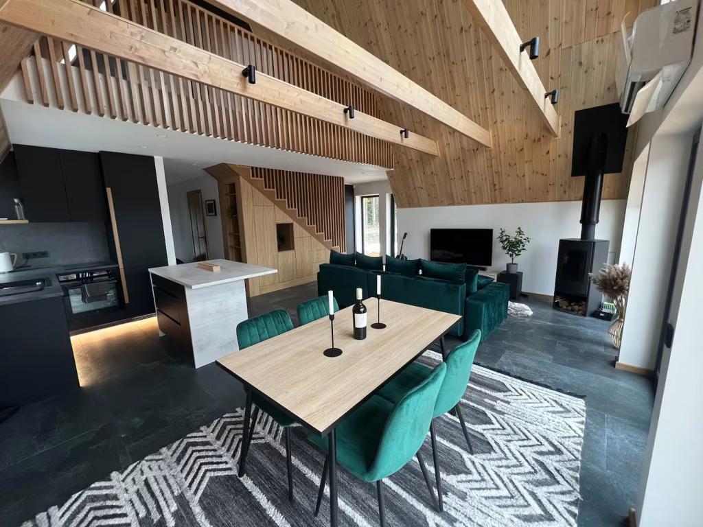 A modern A-frame interior features a black kitchen and emerald green velvet furniture set against light wood-paneled walls and exposed ceiling beams.