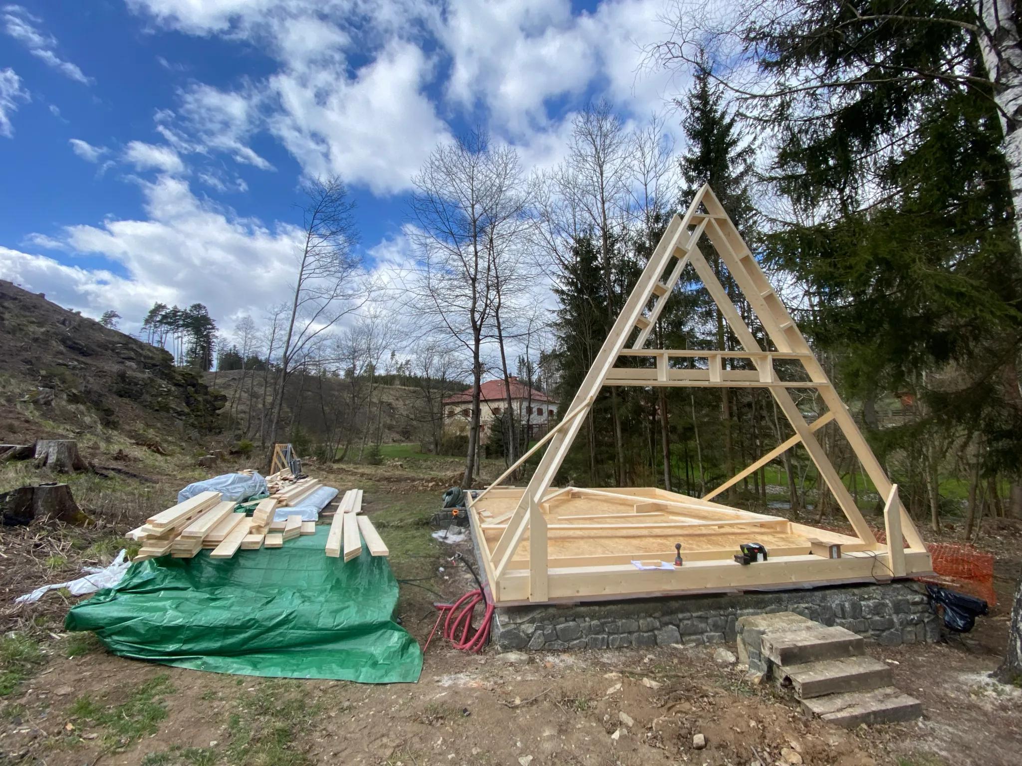 The first timber A-frame truss is erected on a stone foundation, marking the beginning of the structural assembly for a new cabin.