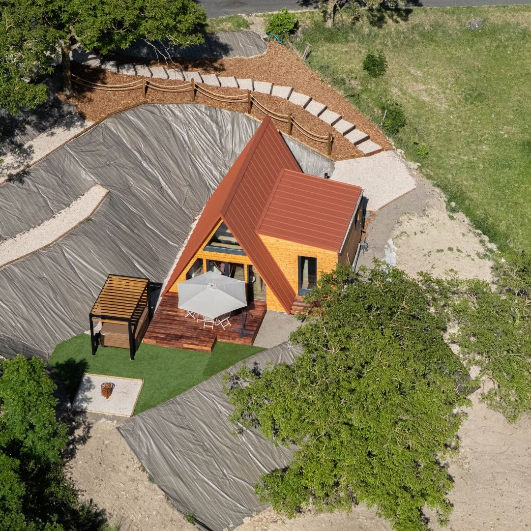 Aerial view of a finished Avrame Duo 75 A-frame house in France with a terrace, outdoor dining area, pergola, and terracotta steel roof
