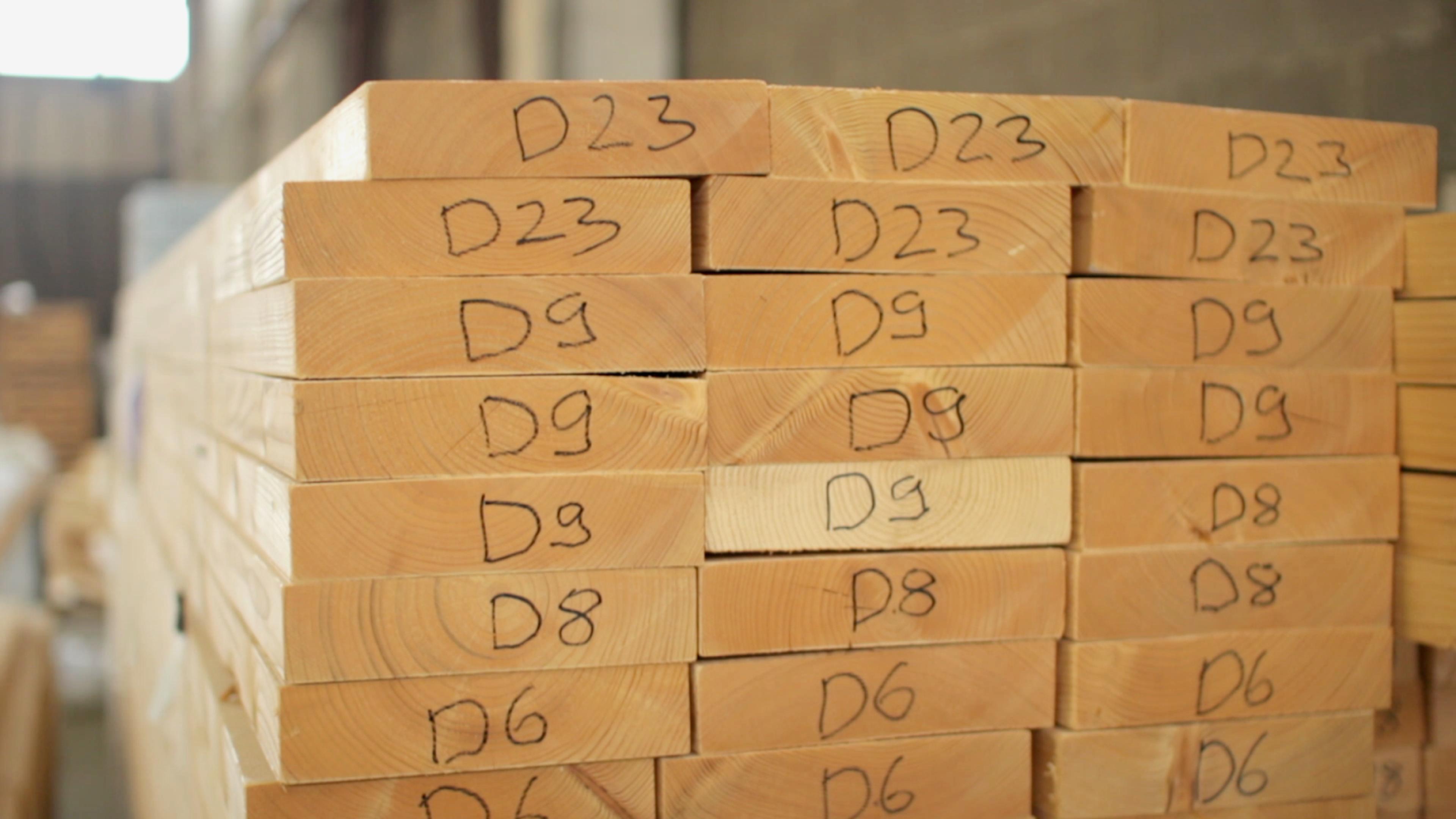 A stack of precision-cut lumber for an Avrame kit is organized in a warehouse, with each piece clearly labeled (e.g., "D23", "D9", "D8") to guide the assembly process.