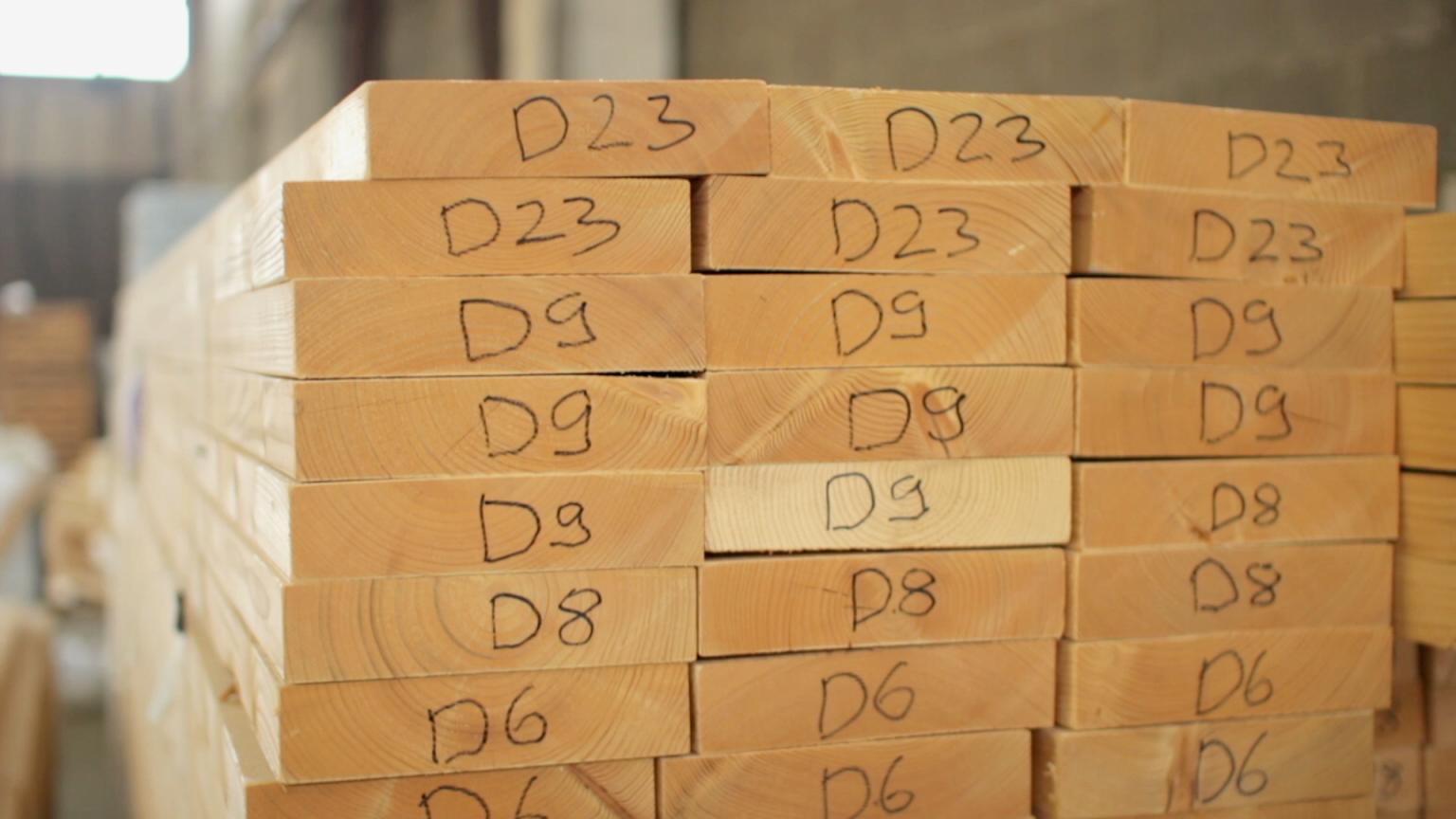A stack of precision-cut lumber for an Avrame kit is organized in a warehouse, with each piece clearly labeled (e.g., "D23", "D9", "D8") to guide the assembly process.