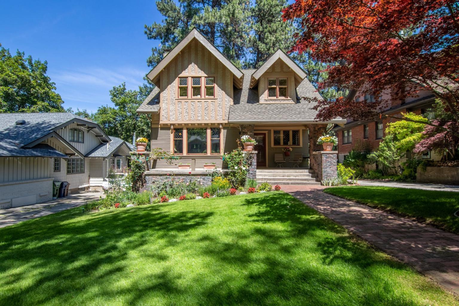 A charming two-story Craftsman-style home features a manicured green lawn, a brick walkway, and classic architectural details under a clear blue sky.