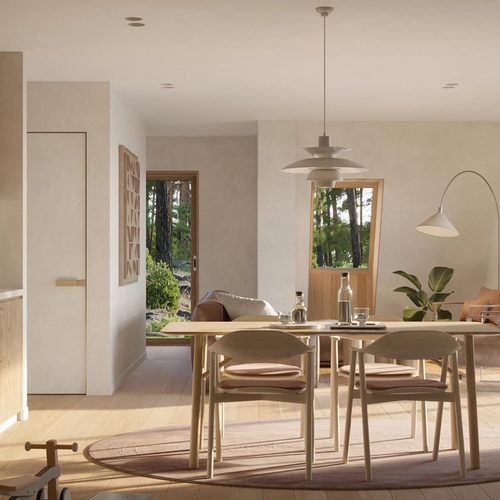 A minimalist A-frame interior features light oak cabinetry and furniture in an open-concept living and dining space that looks out onto a dense forest through large glass doors.