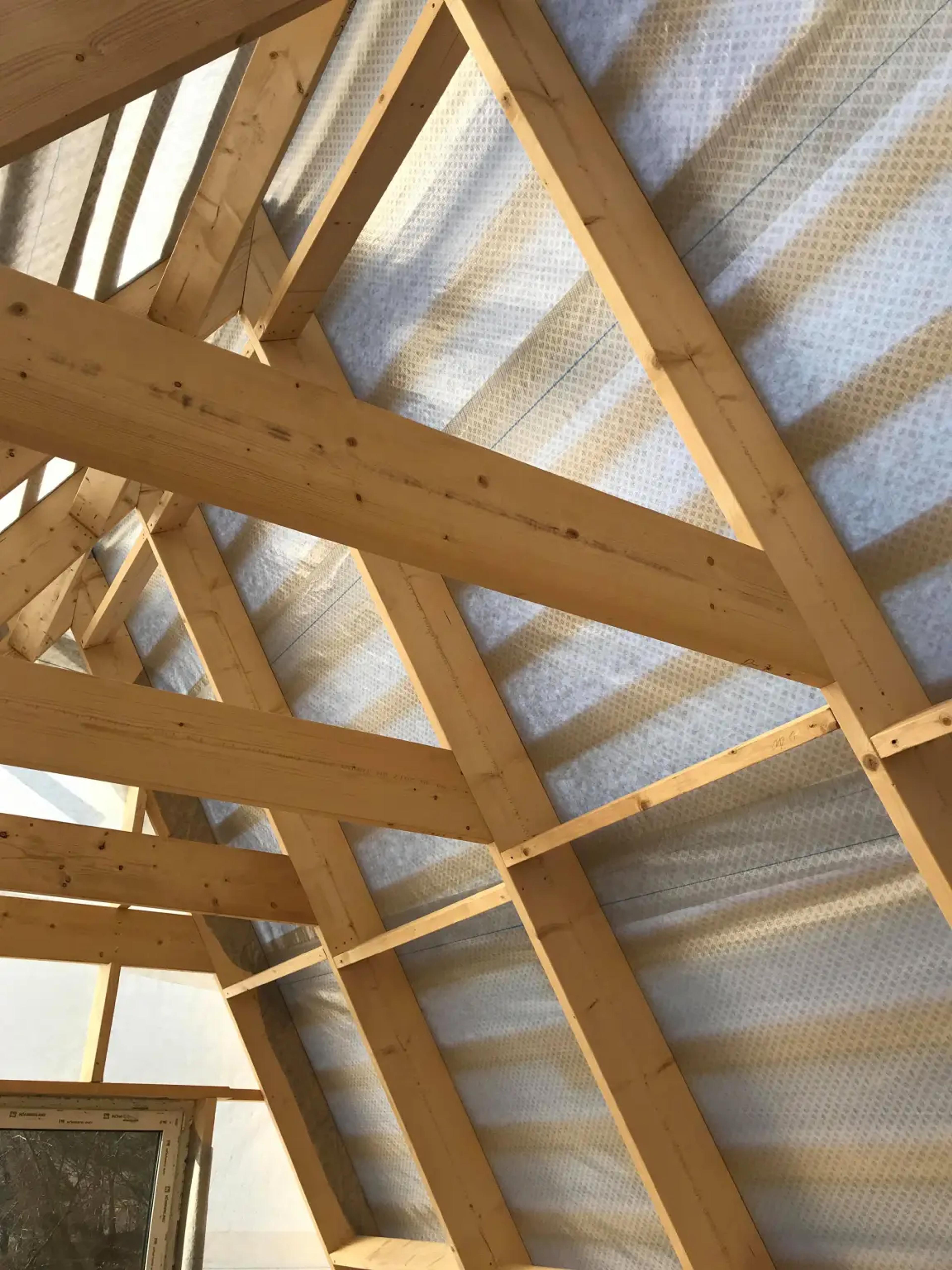 The interior wooden structural frame of an A-frame house is shown with a translucent weather-resistant membrane installed over the rafters.