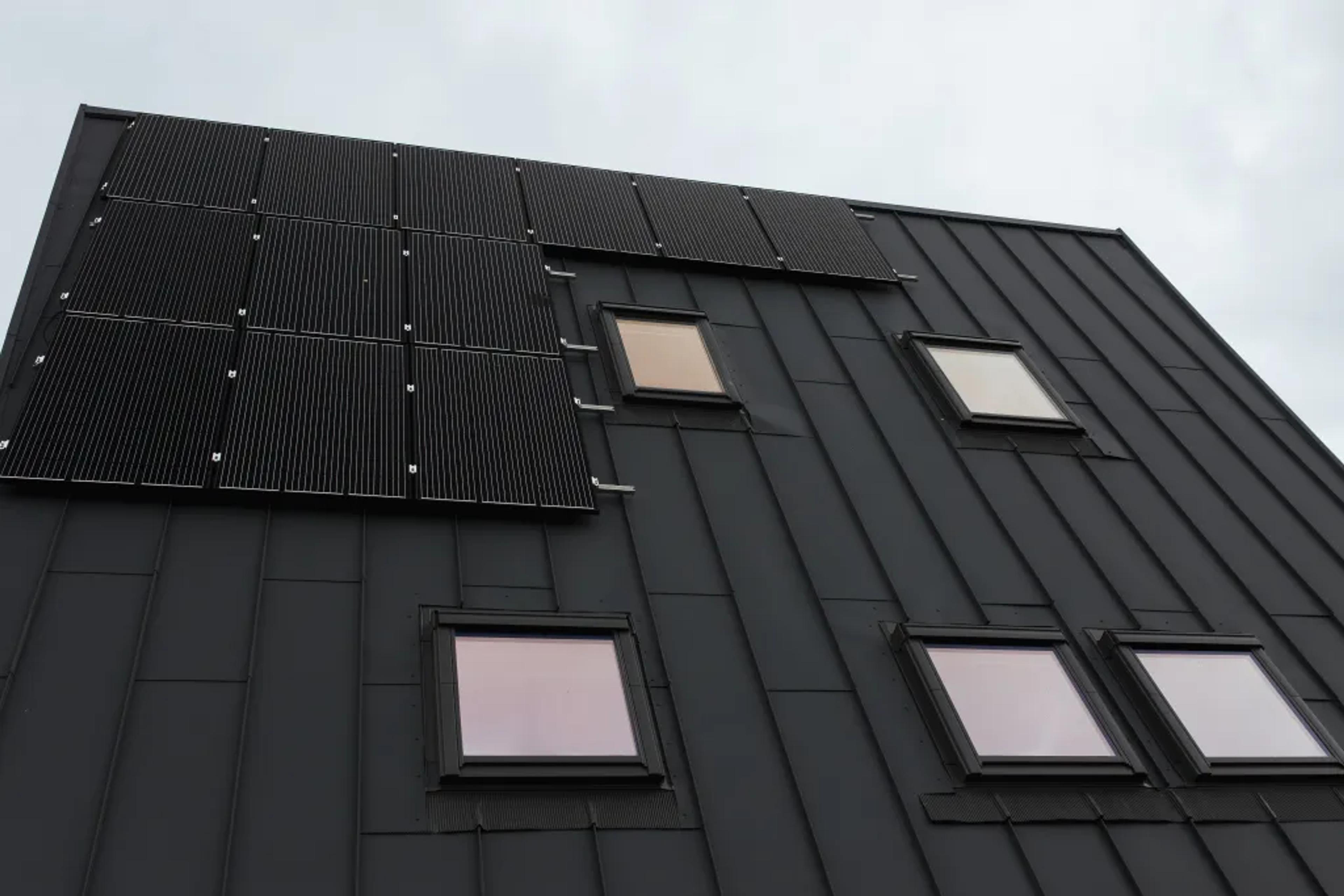 A close-up view of a dark metal standing-seam roof shows several integrated solar panels and multiple square skylights.