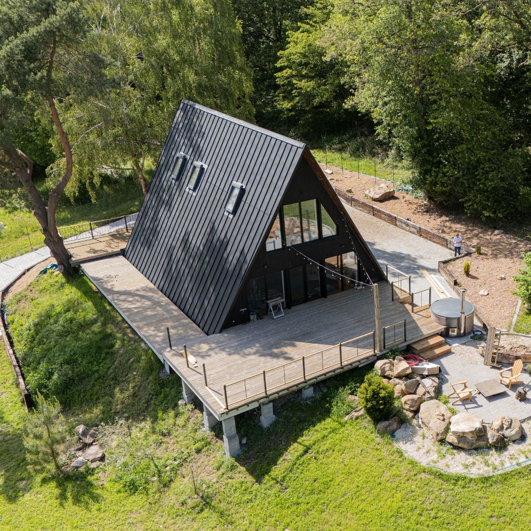Avrame Trio 120 and Duo 57 A-frame houses under construction in northern France, exterior clad in dark timber with large windows, surrounded by trees