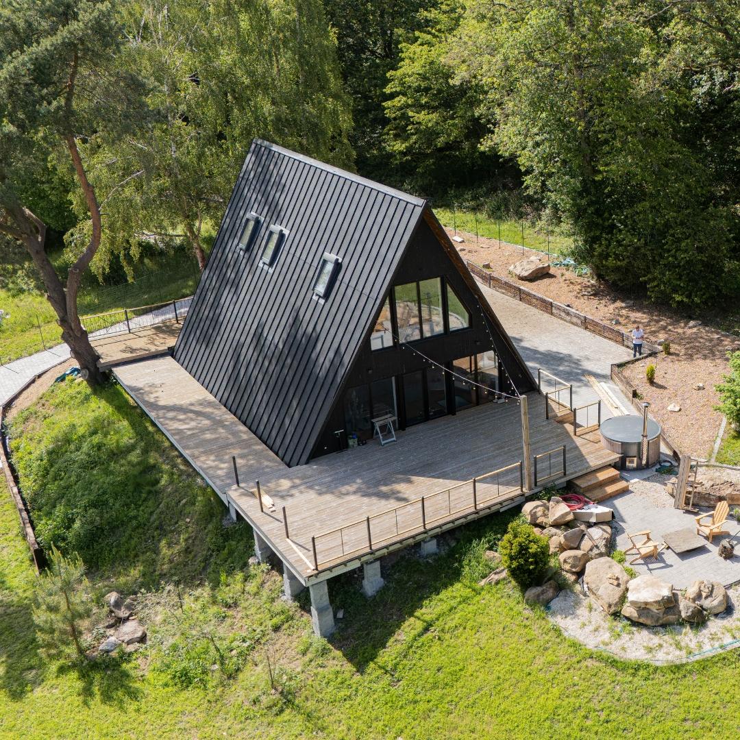 Avrame Trio 120 and Duo 57 A-frame houses under construction in northern France, exterior clad in dark timber with large windows, surrounded by trees
