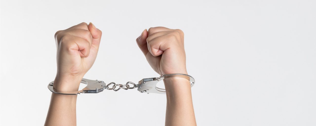 A pair of clenched fists are raised against a plain white background while bound together by metal handcuffs.
