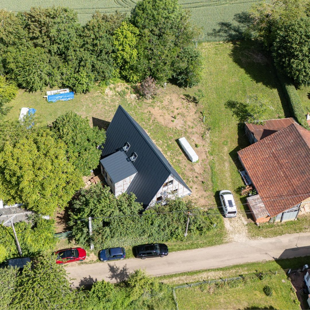 Aerial view of an Avrame Trio 150 A-frame house under construction in the French countryside, with dark steel roof cladding partially installed