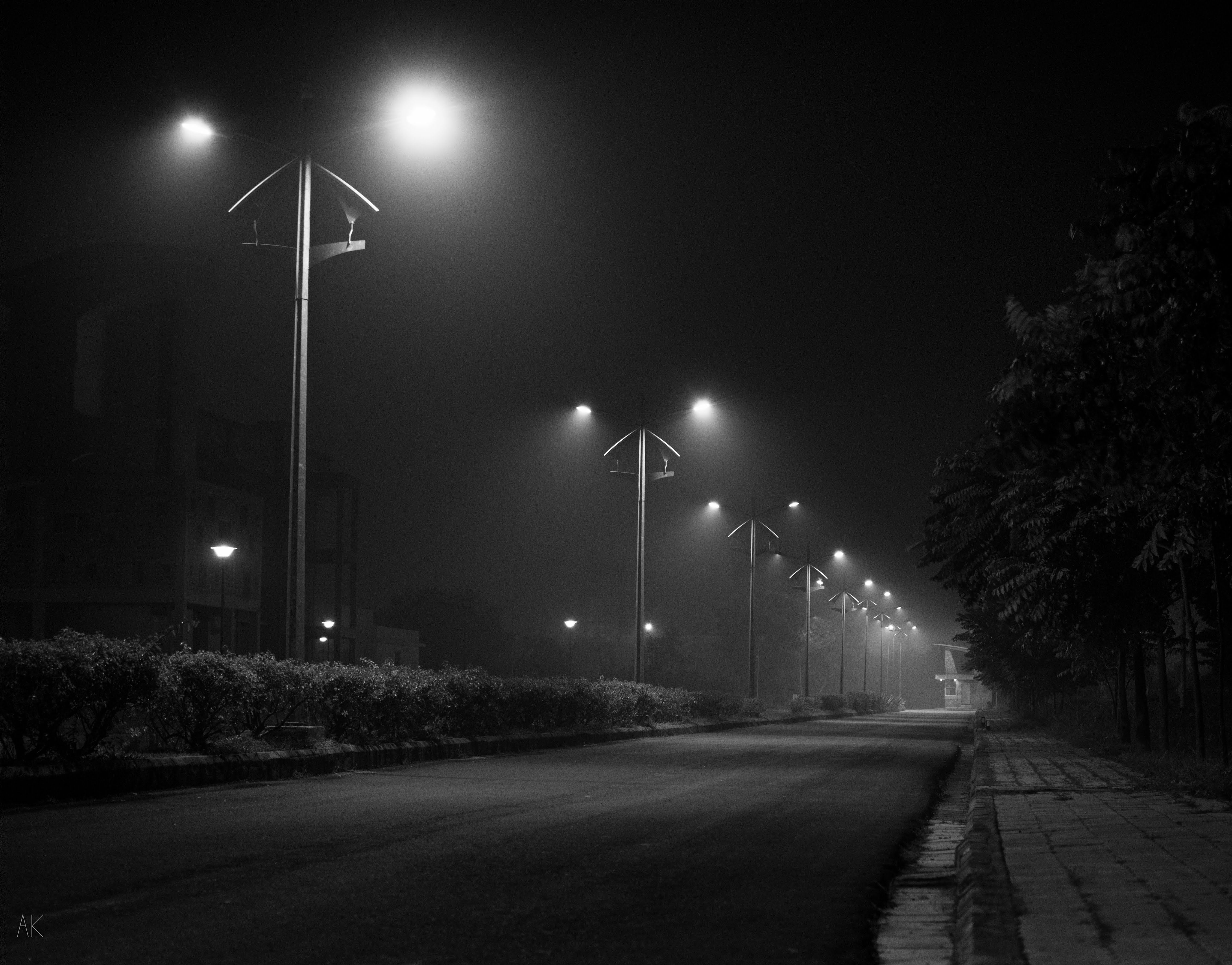 Empty road at night under fog, street lamps receding into the distance.