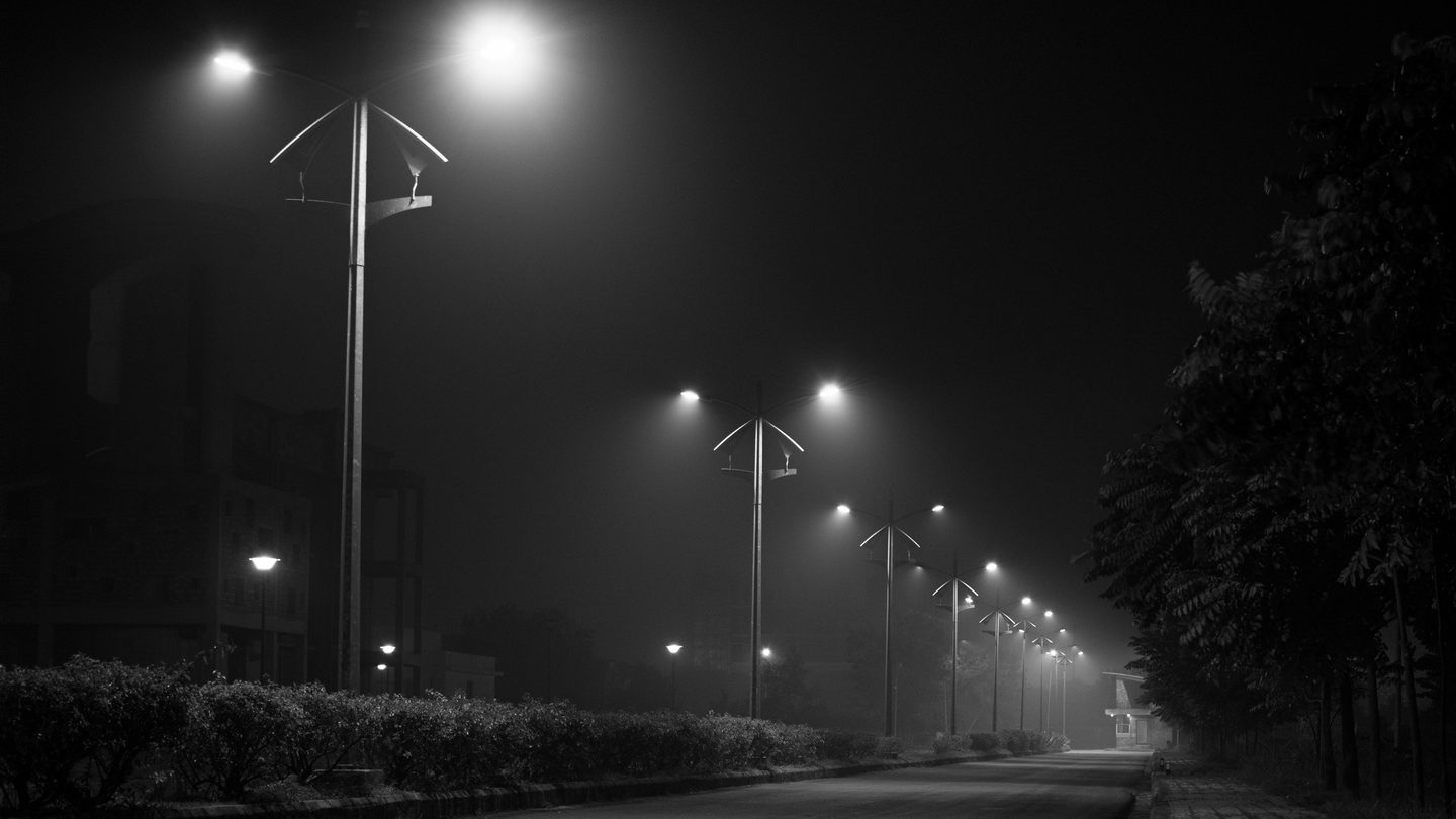 Empty road at night under fog, street lamps receding into the distance.