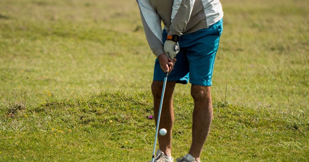 Mature golfer in white shirt and red cap playing a round on the course