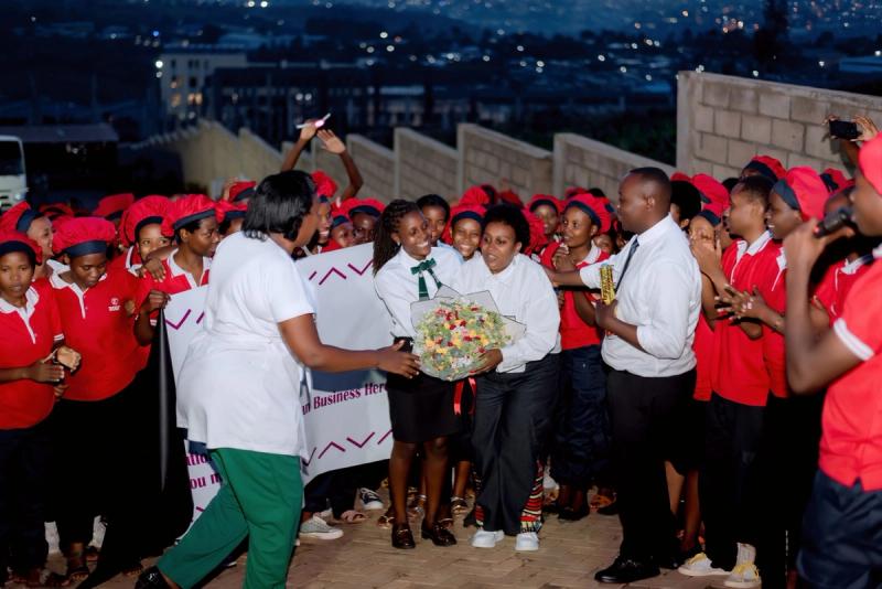 Diane Mukasahaha receives a bouquet from DIKAM staff during the night-time celebration, with Kigali's lights behind