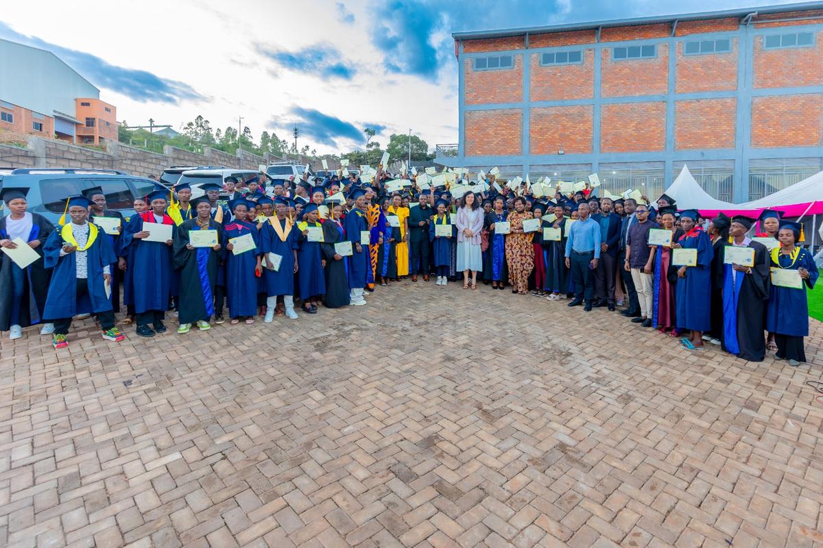 Graduates of the DIKAM Training Center in caps and gowns, holding their certificates in front of the factory