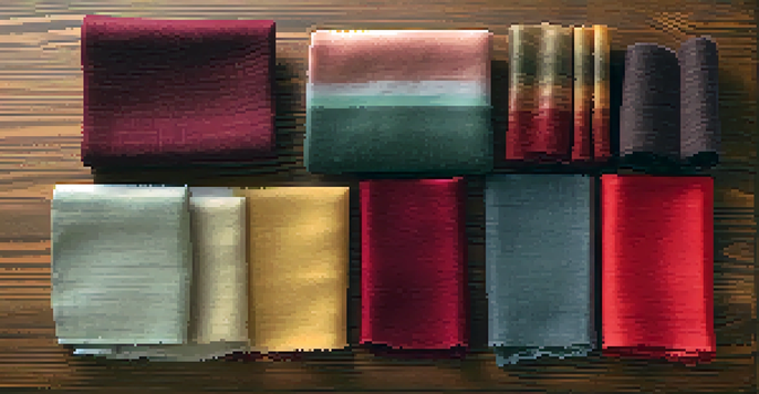 A flat lay of different fabric swatches including silk, cotton, and wool in various colors on a wooden table, with soft natural light illuminating the textures.