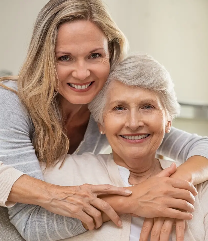 older woman smiling while being hugged from behind by young woman