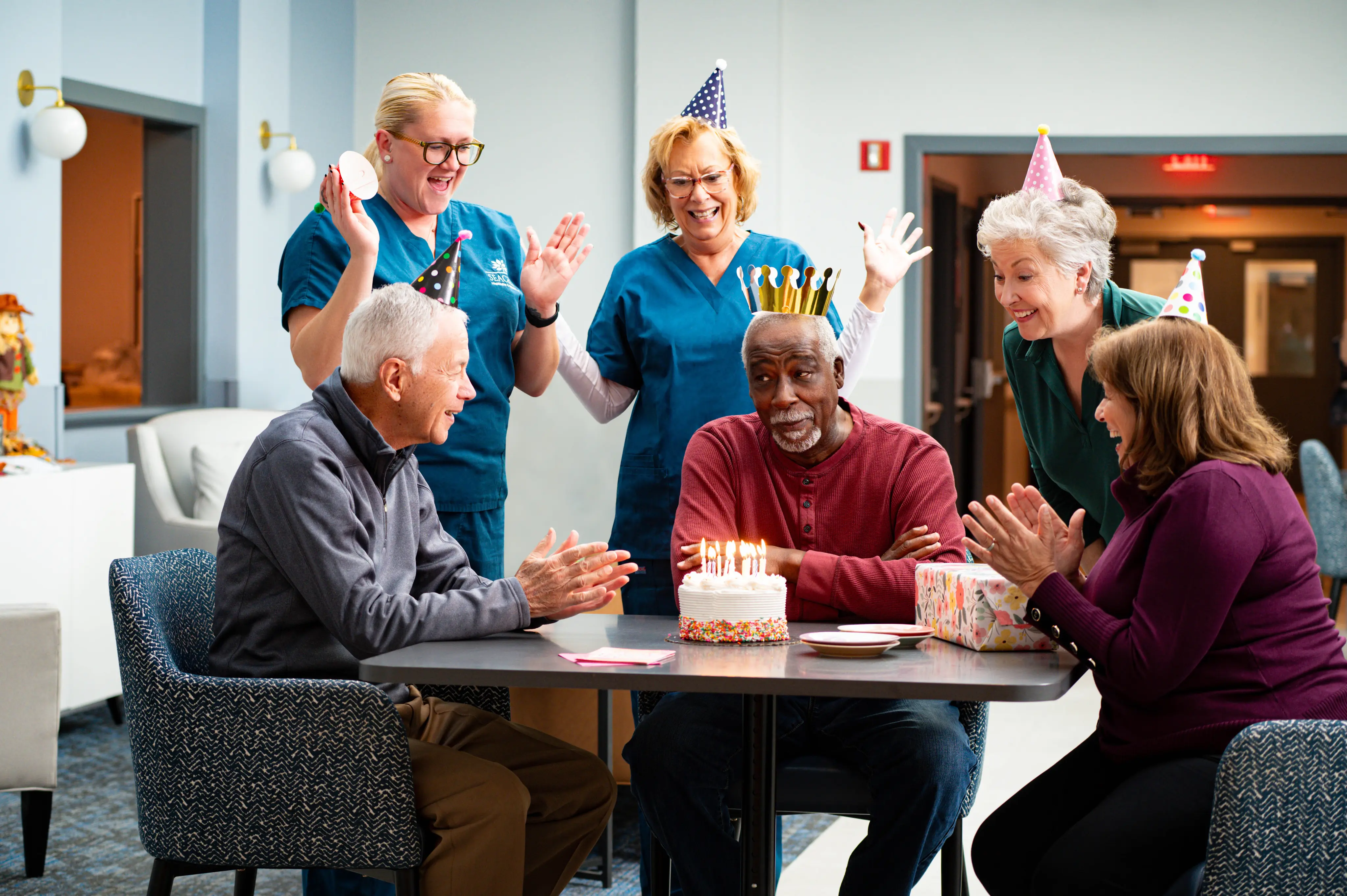 older adults celebrating a man's birthday with nurses in a senior living home