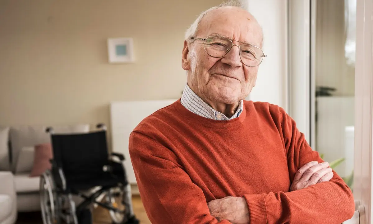 older man smiling in front of an empty wheelchair